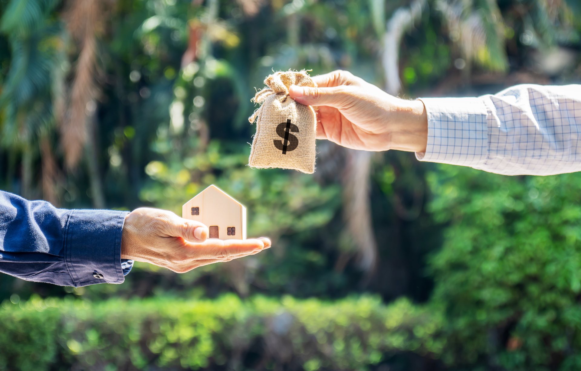 Small wooden house being held by someone with a blue shirt and a money bag being held by someone wearing a plad shirt
