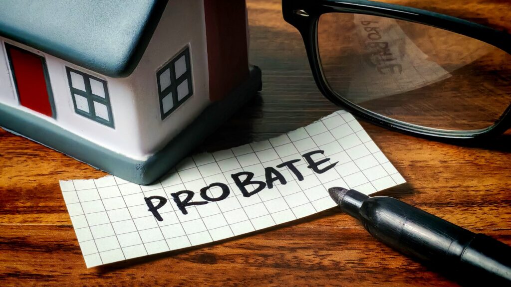 a little wooden house next to glasses, a pen, and a sign that says probate