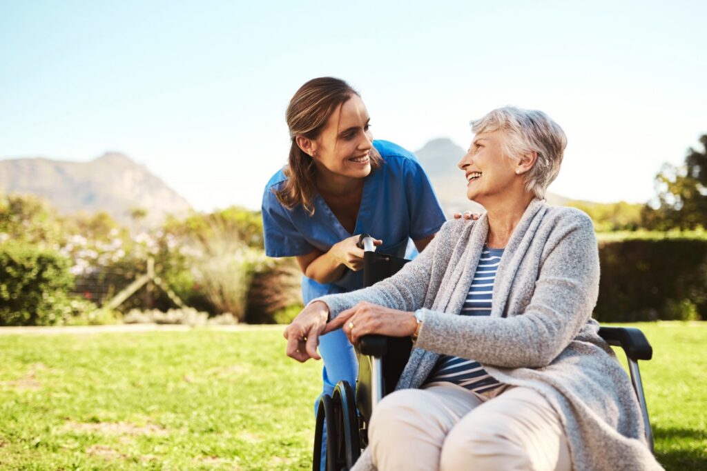 Older woman in a wheelchair with a woman in a blue outfit leaning over her talking to her
