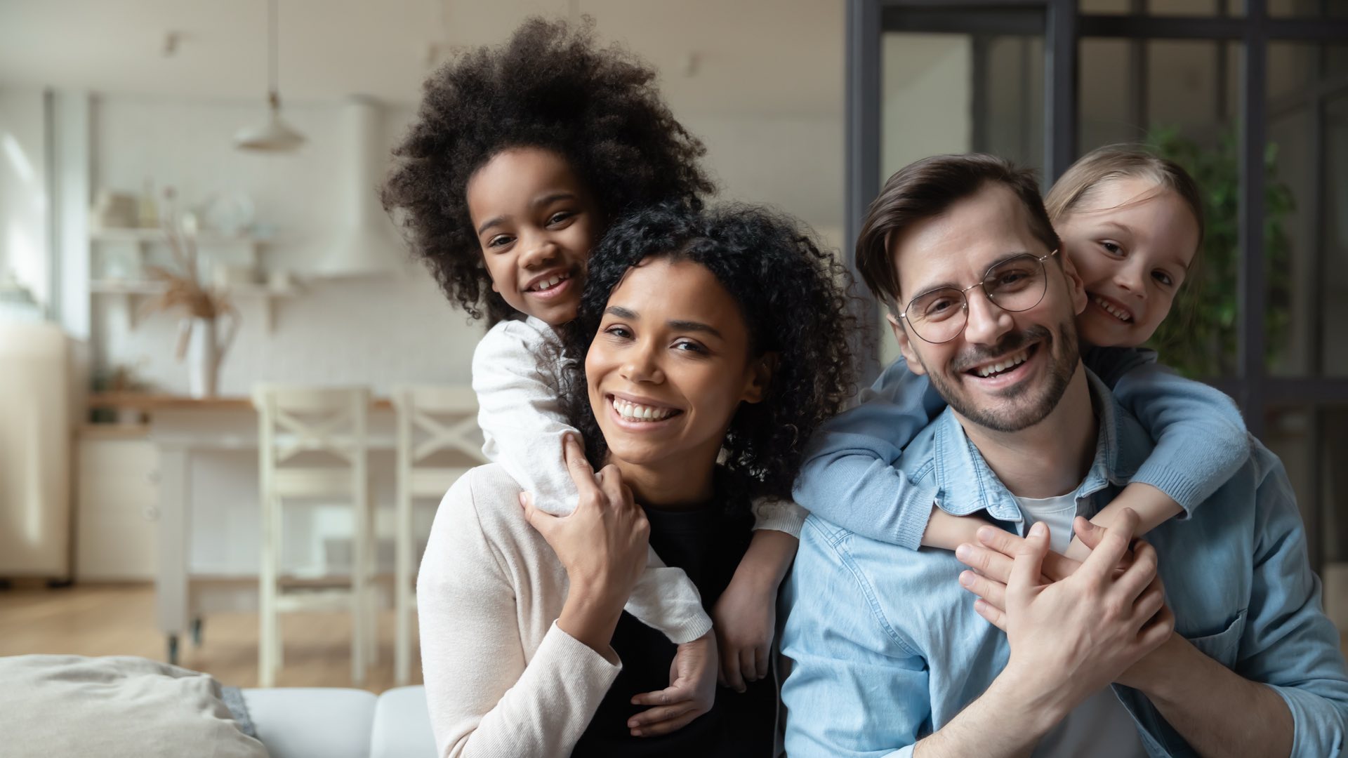 Multiracial couple enjoying sweet family moment with two small children on their backs